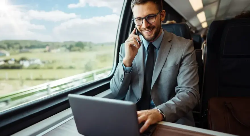 Biznesmen w garniturze rozmawia przez telefon i pracuje na laptopie w pociągu.