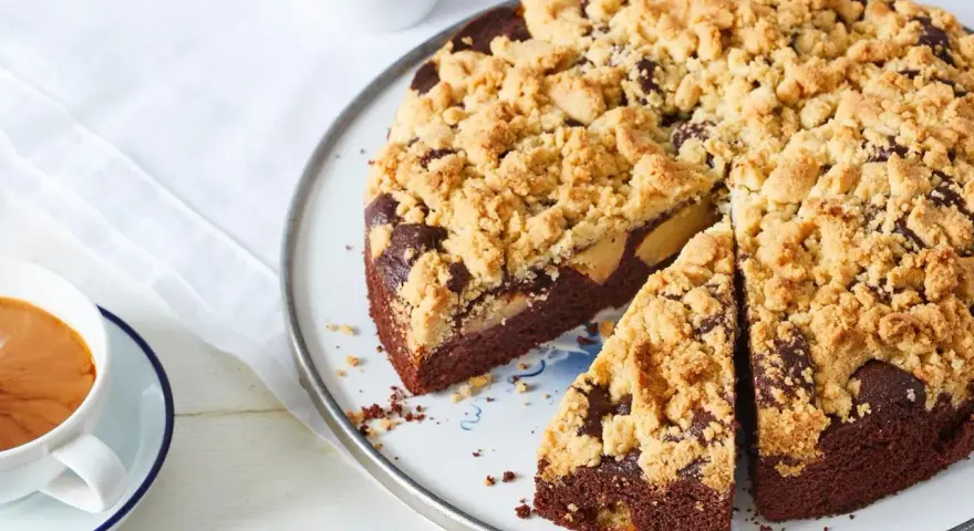 Ein saftiger Apfel Schokoladenkuchen mit knuspriger Streuseldecke, daneben eine Tasse Kaffee.