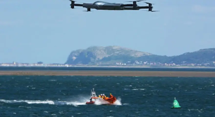 Search and rescue drones hover over a lifeboat speeding across choppy waters, assisting in a coastal operation.