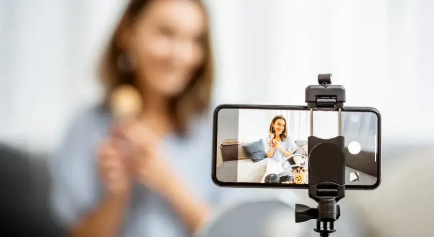 Kobieta nagrywa filmik telefonem komórkowym, trzymając pędzel do makijażu.