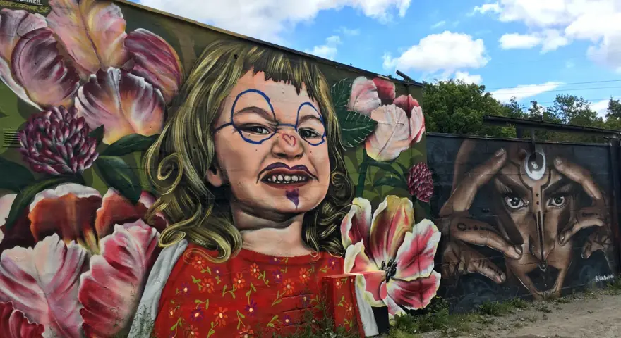 En väggmålning med en busig flicka omgiven av blommor ger graffiti inspiration. Bredvid syns ett mystiskt ansikte med händer.