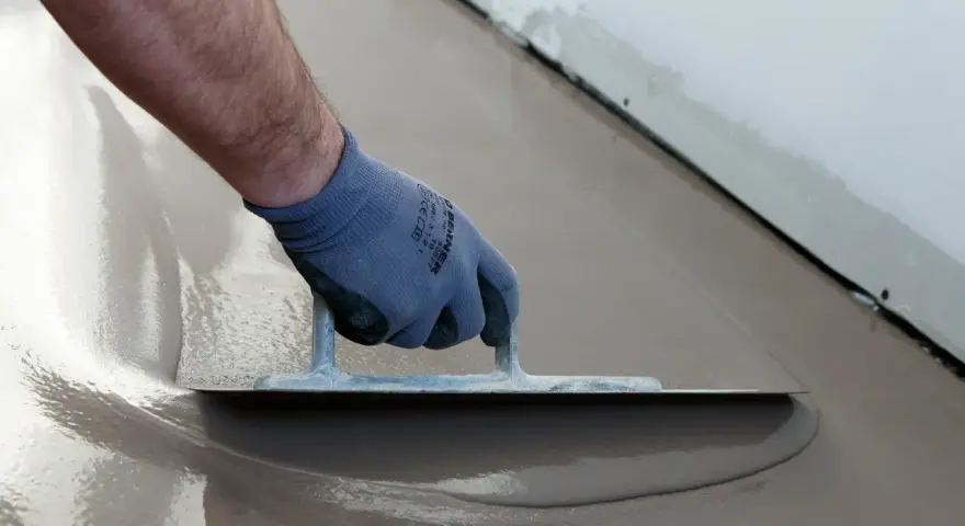 Hand med handske spacklar betonggolv med en bred spackel.