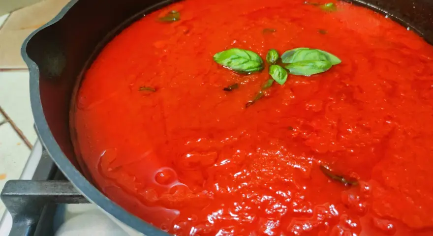 Sugo al pomodoro fresco e profumato, con foglie di basilico che galleggiano in una padella di ghisa.