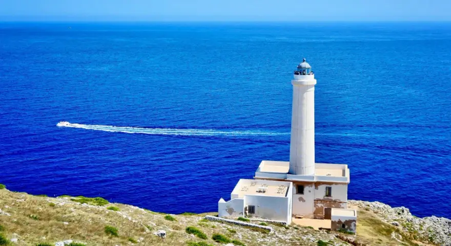 Faro di Punta Palascìa, uno dei luoghi da vedere a Otranto, con il mare blu e una barca in lontananza.