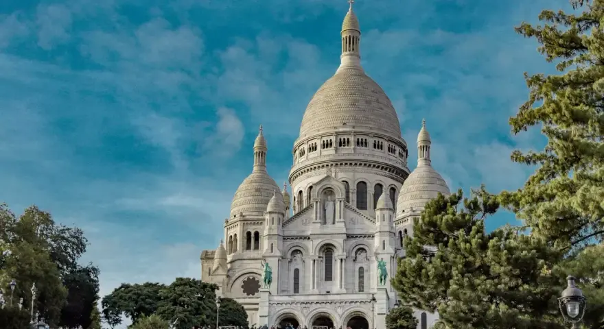 Basílica del Sacré-Cœur, uno de los monumentos de Francia, se alza majestuosa bajo un cielo azul con nubes.