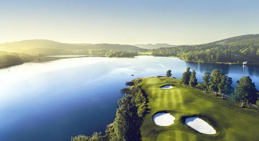 Vacker golfbana vid en sjö, perfekt för norsk golf. Grönskande kullar och solnedgång.
