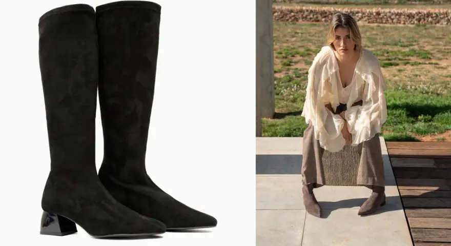 Botas negras de altura de caña con tacón brillante, combinadas con una mujer con falda y blusa voluminosa sentada al aire libre.