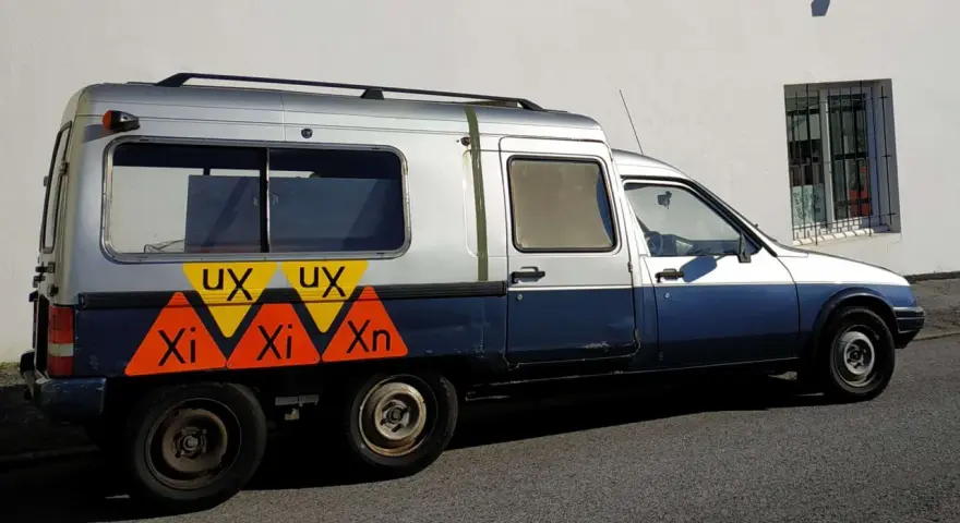 Dwukolorowy Citroen C15 z nietypowymi oznaczeniami "UX" i "Xi Xn" na boku, zaparkowany przy białej ścianie.