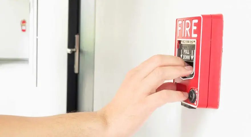 Mano activando la alarma de incendios. Instrucciones claras: "PULL DOWN" para saber cómo apagar alarma de incendios.