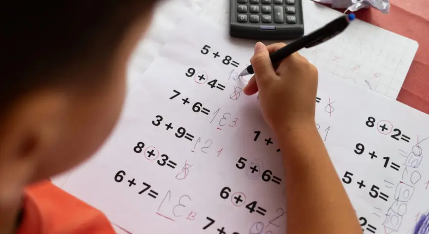 Dziecko rozwiązuje zadania matematyczne, próbując pokonać dyskalkulię. Widoczny kalkulator i zeszyt sugerują naukę.
