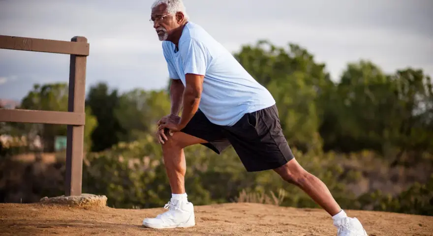 Un homme âgé s'étire pour muscler ses cuisses, un exercice simple en extérieur.