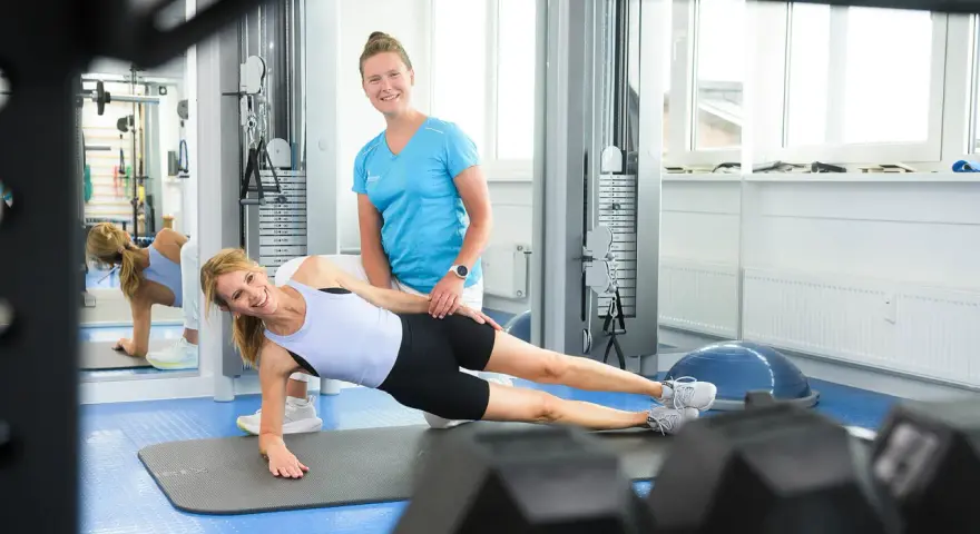 Physio-Übung: Frau macht Seitenstütz, Therapeutin hilft.