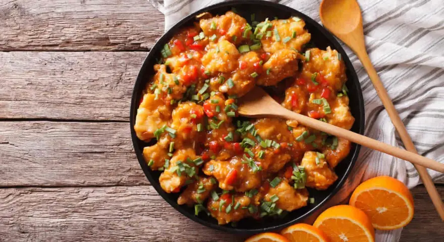 Sabroso pollo a la naranja, cubierto con salsa brillante y cebollín picado, servido con rodajas de naranja fresca.
