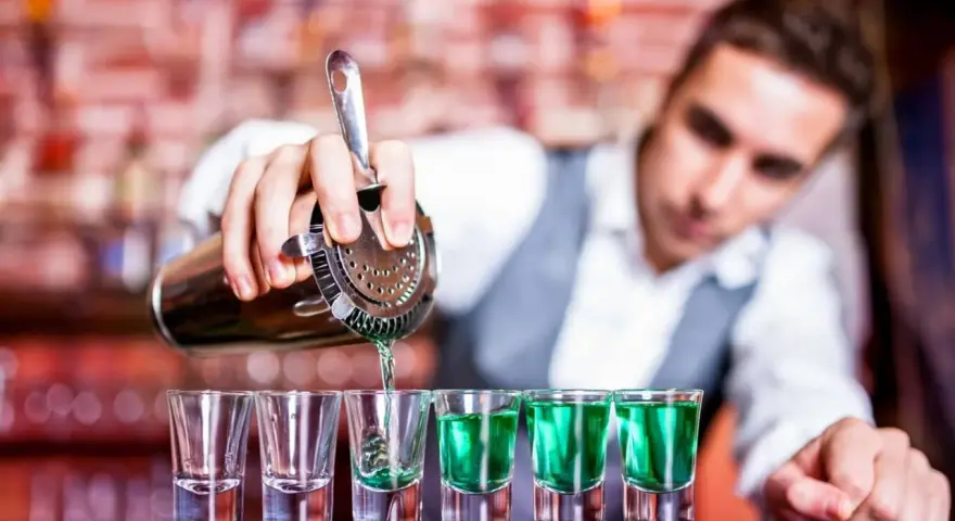 Barman nalewa zielony shot. Zastanawiasz się, ile kosztuje kurs barmana? To inwestycja w przyszłość!