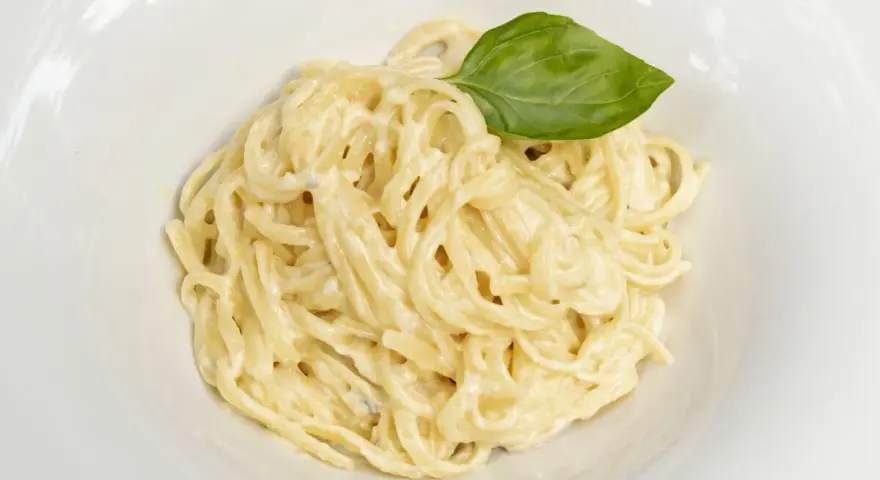 Un plato de spaghetti a la carbonara con nata, cremoso y adornado con una hoja de albahaca fresca.