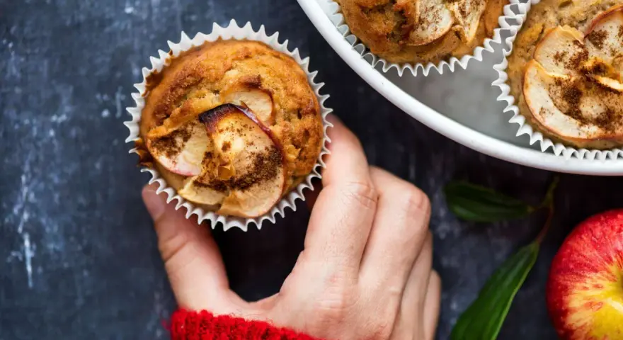 Hand hält einen frisch gebackenen Apfelmuffin, bestreut mit Zimt. Ein tolles Apfelmuffins Rezept!