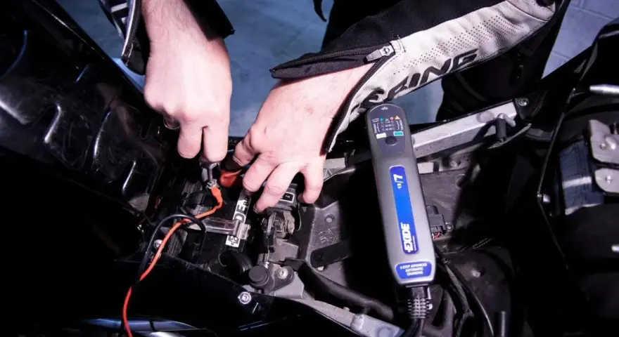 Mani che collegano un caricabatterie Exide alla batteria di una moto, per risolvere il problema della batteria si scarica a moto ferma.