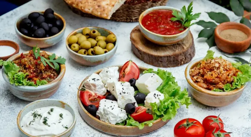 Un banchetto di piatti tipici grecia: feta fresca, olive nere e verdi, salsa di pomodoro, melanzane e pane pita.