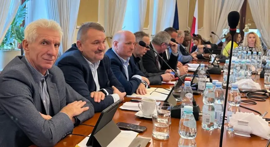 Mężczyźni przy stole obradują, dyskutując o przyznaniu absolutorium.