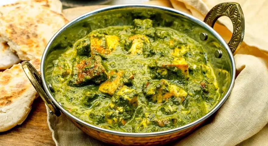 Ein köstliches Palak Paneer in einer Kupferschale, serviert mit Fladenbrot und Chiliflocken.