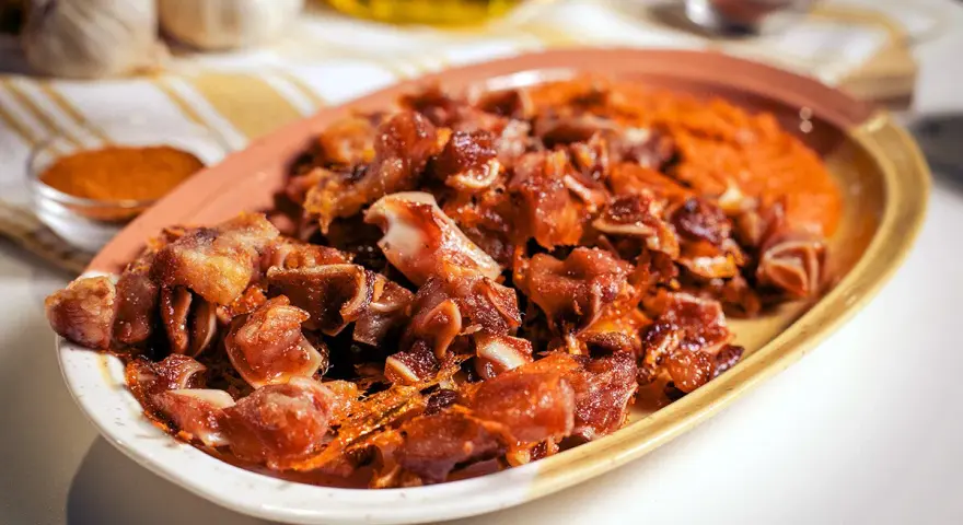 Oreja de cerdo crujiente y dorada servida en un plato con puré naranja.