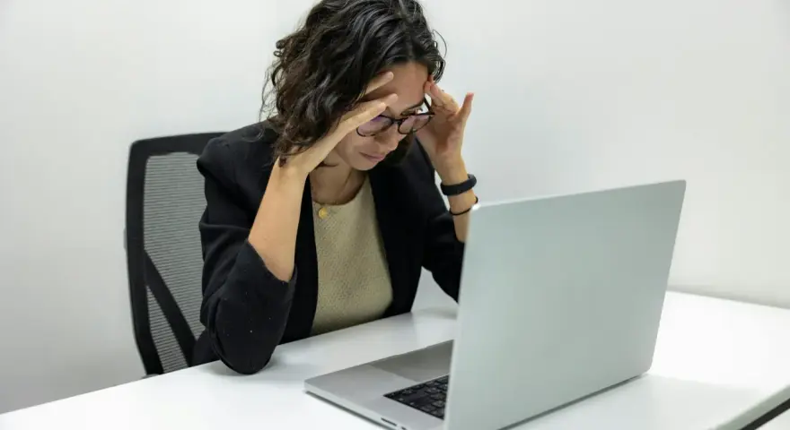 Femme stressée devant son ordinateur, les mains sur les tempes. Une situation difficile, peut-être un licenciement pendant arrêt maladie pour dépression.