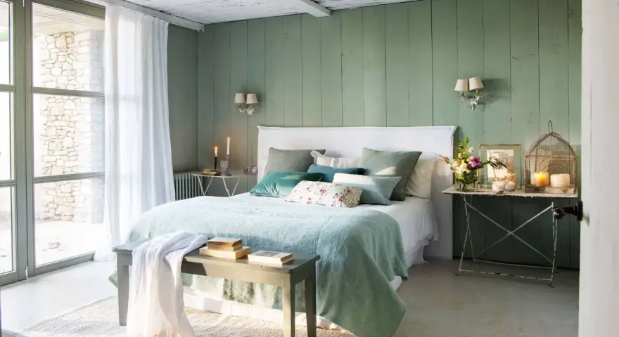 Acogedor dormitorio verde agua y blanco con cama mullida, cojines y luz natural.