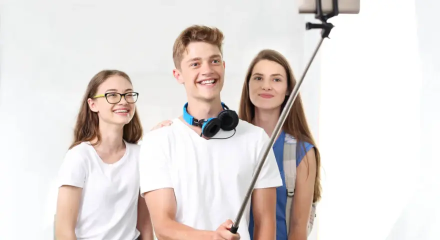 Trzech przyjaciół robi sobie selfie na kijku. Chłopak z przodu uśmiecha się szeroko, pokazując, jak robić zdjęcia.