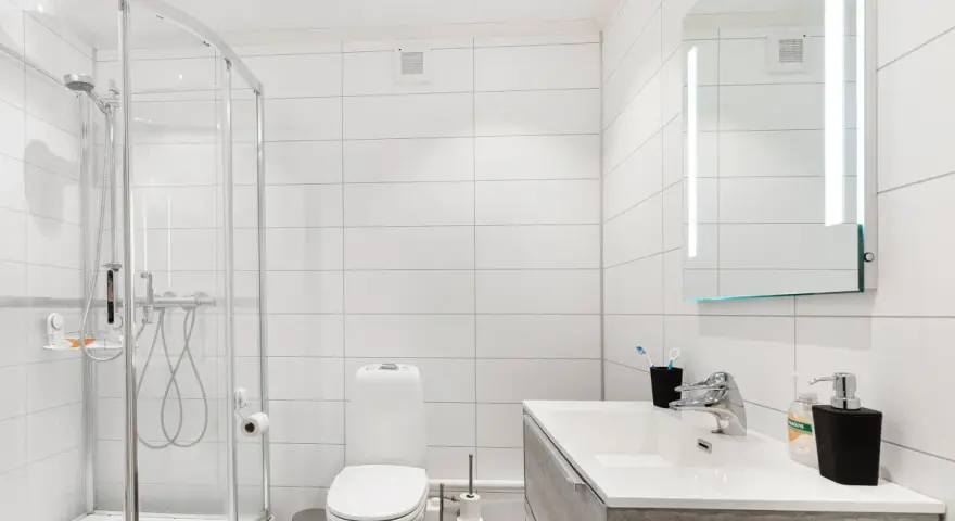 Baño moderno con ducha, inodoro y lavabo. La ventilación del baño es discreta en la pared, asegurando un ambiente fresco.