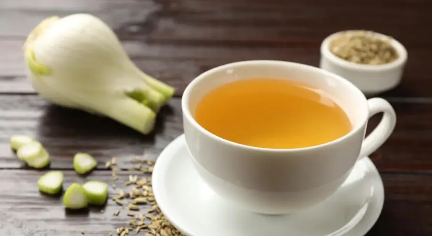 Una taza de infusión de hinojo por la noche, con hinojo fresco y semillas esparcidas.