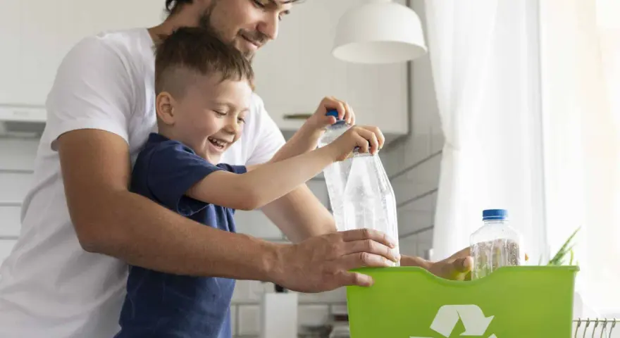 Padre e hijo reciclando botellas de plástico en un contenedor verde. Enseñando conciencia ecológica desde pequeños.