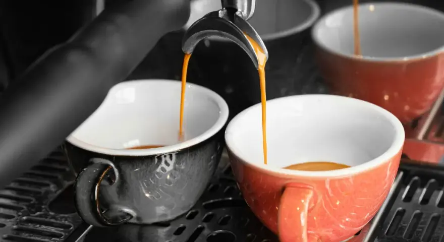 Dwie filiżanki, jedna szara, druga pomarańczowa, napełniają się aromatyczną kawą doppio.
