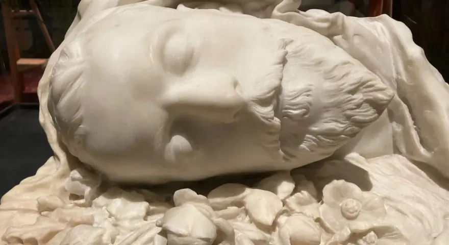 Sculpture en marbre d'un visage endormi, entouré de fleurs. Une œuvre d'art évoquant la célèbre Sarah Bernhardt.