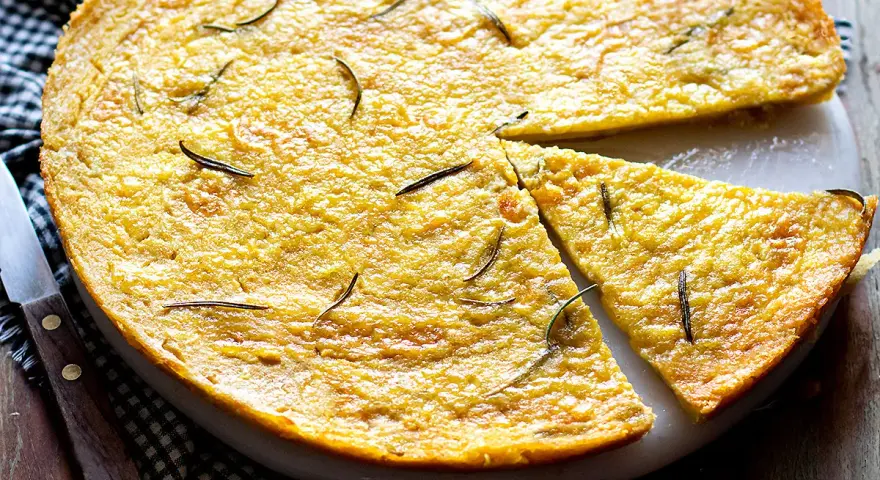 Una torta dorata, profumata al rosmarino, perfetta come ricetta con farina di ceci. Una fetta è già stata tagliata.