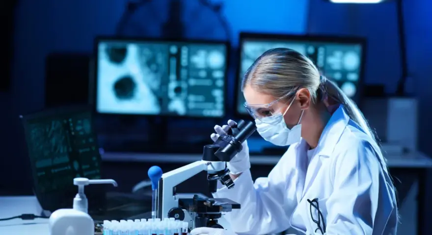 Kto pracuje w laboratorium medycznym? Młoda kobieta w okularach i masce, analizująca próbki pod mikroskopem.