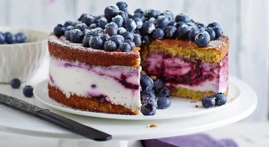 Saftige Heidelbeertorte mit Joghurt-Füllung, garniert mit frischen Beeren und Puderzucker. Ein Genuss für Augen und Gaumen.