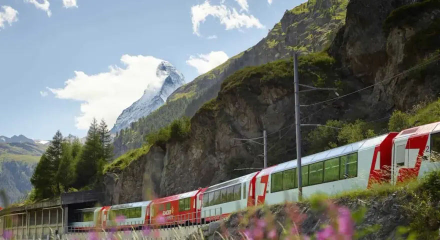 A red and white Glacier Express train travels through the Swiss Alps, with the Matterhorn in the background, on its scenic journey from Zermatt to Andermatt.