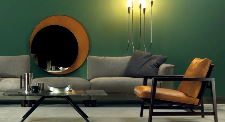 Elegante soggiorno con divano grigio, poltrona in pelle color cuoio e specchio rotondo. Idee su come abbinare divano e poltrone diverse.