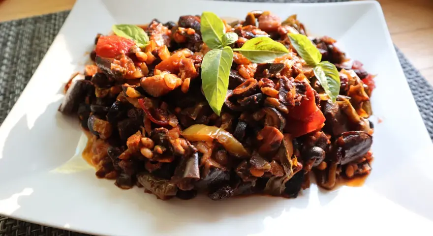Un piatto di saporita caponata di melanzane, guarnita con foglie di basilico fresco.