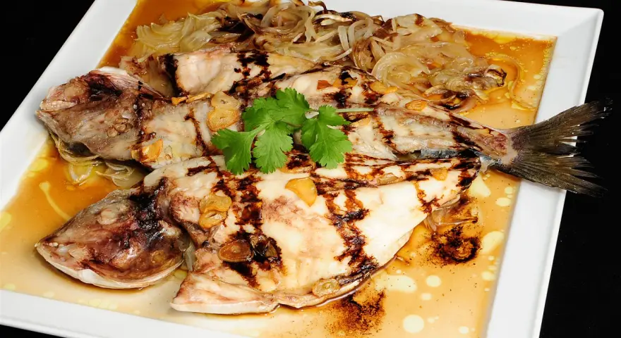 Dorada a la espalda, a la parrilla, con láminas de ajo y cebolla caramelizada, servida en salsa dorada.