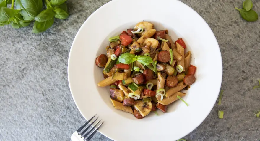 En tallrik med chorizo pasta med grönsaker som paprika, zucchini och champinjoner. Garnerad med färsk basilika och salladslök.