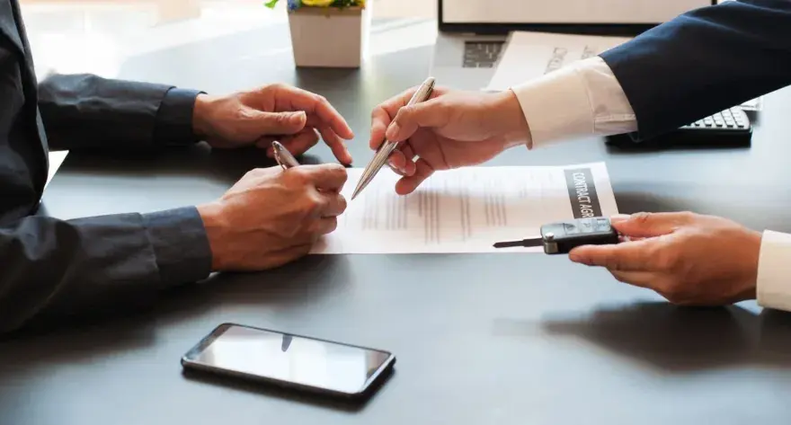 Deux hommes signent un contrat, l'un remettant les clés d'un véhicule. Une transaction pour un **gapd bail commercial** est en cours.