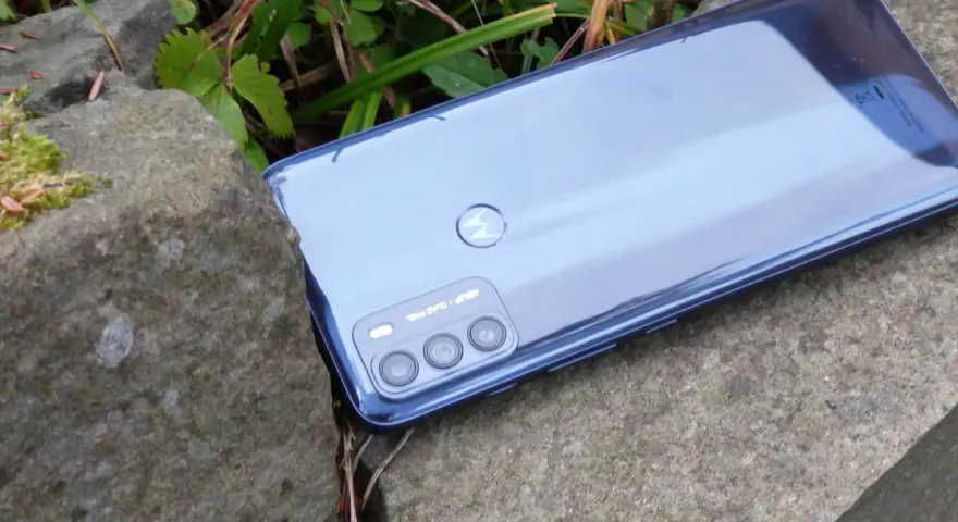 Błyszczący tył telefonu **Moto G 50** z potrójnym aparatem, leżący na kamieniach wśród zieleni.