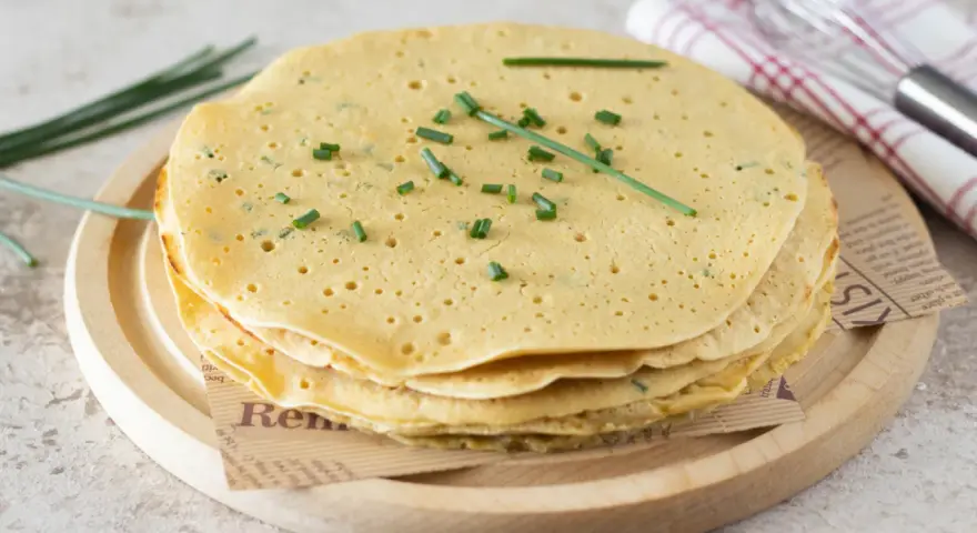 Pila di piadine di ceci dorate, guarnite con erba cipollina fresca. Perfette per un pasto leggero e gustoso.