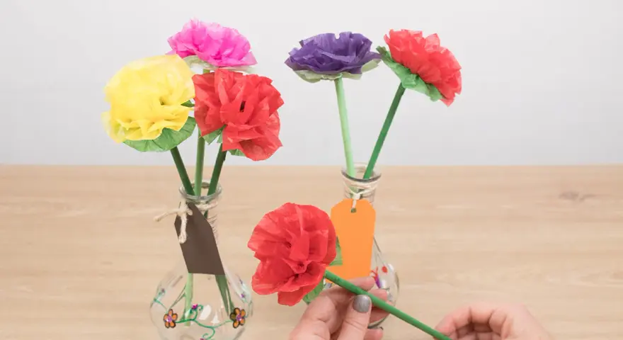 Flores de colores hechas con manualidades de papel de seda, en jarrones decorados.