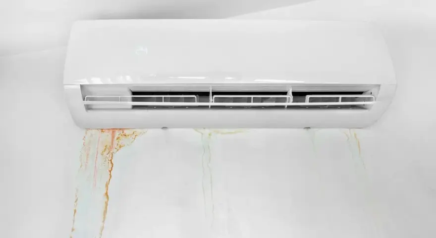 Condizionatore bianco con macchie d'acqua sul muro. La condensa gocciola, creando aloni color ruggine e verdognoli.