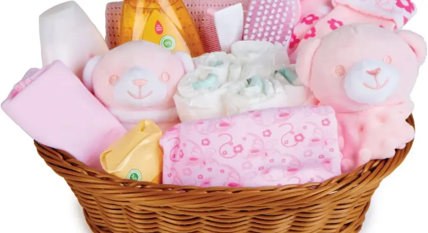 En korg fylld med rosa babyartiklar, inklusive nallar, blöjor och tvättlappar, perfekt som baby shower present.