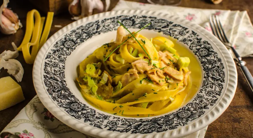 Makaron tagliatelle w kremowym sosie curry z kurczakiem i porem, ozdobiony szczypiorkiem.