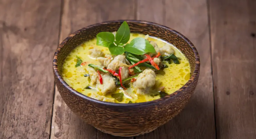 Zielone curry z kurczakiem i chili w drewnianej misce na desce.