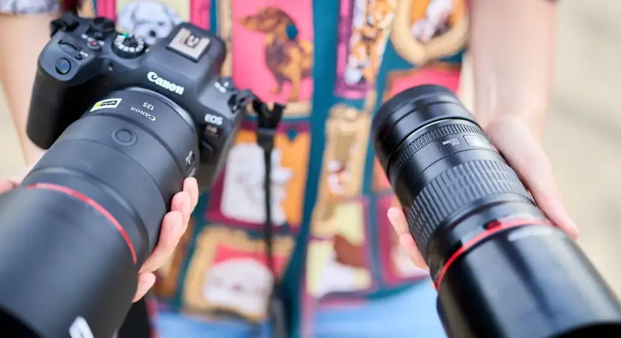 Dwie ręce trzymają obiektywy do Canona. Jeden z nich to Canon RF 135mm f/1.8L IS USM, drugi to Canon EF 135mm f/2L USM.